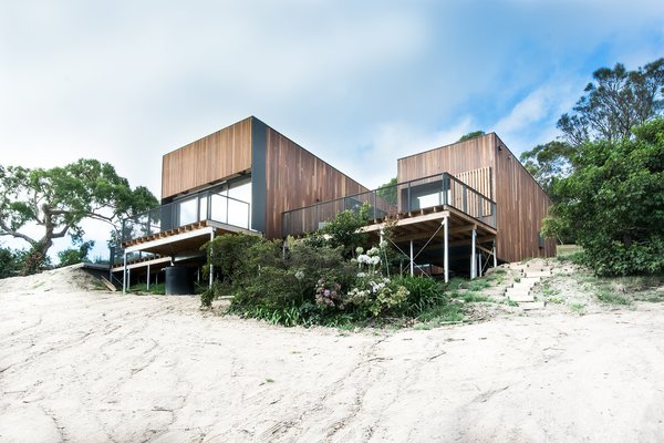 The home, clad in natural Australian timber, enjoys a sense of lightness thanks to slender columns that let it float over the dunes. The driveway and entry, at the rear of the building, have an understated design to build to the interior's magnificent ocean views. Firm director Phil Snowdon explains, “By creating an architectural form that draws your eye and leads you up the steep driveway, we could engage new visitors in a welcoming process that first reveals the object and then slowly reveals the main event, being the view." Photo of Martha modern home