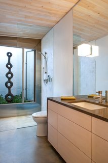 A Toto toilet and bathroom sink, with a faucet by GROHE, are illuminated by a Leucos light fixture. Birgit Piskor designed the sculpture in the garden beside the shower.