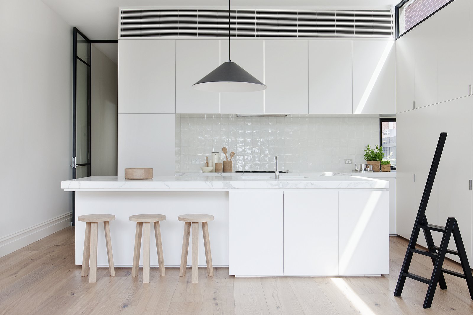 Faced with size constraints in the kitchen area—the designers were unable to build above 10 feet on the West facing side of the house—Robson and Cohen installed delicate steel clerestory windows which add extra illumination. A black Aggregato Saliscendi Suspension light, designed by Enzo Mari and Giancarlo Fassina for Artemide, accents against white honed Calacatta marble countertops and MAP's oak Milky Stools.