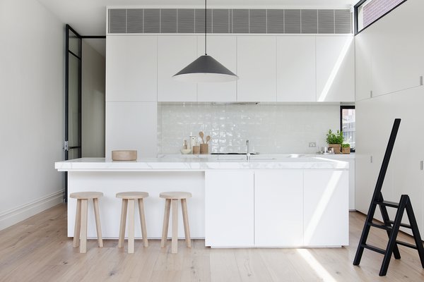 Faced with size constraints in the kitchen area—the designers were unable to build above 10 feet on the West facing side of the house—Robson and Cohen installed delicate steel clerestory windows which add extra illumination. A black Aggregato Saliscendi Suspension light, designed by Enzo Mari and Giancarlo Fassina for Artemide, accents against white honed Calacatta marble countertops and MAP's oak Milky Stools. Photo 4 of Seclusion modern home