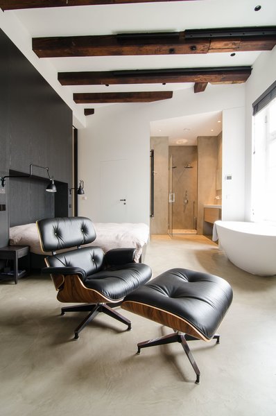 When planning the renovation, the owner gave Standard Studio complete freedom to develop the design. In the unconventional bedroom, the bed sits against a black feature wall, with a prominent freestanding bathtub on the opposite side. In addition to the wood beams, all original windows from the old sugar refinery were preserved, to keep the "soul" of the building intact. Photo 3 of Bloemgracht modern home