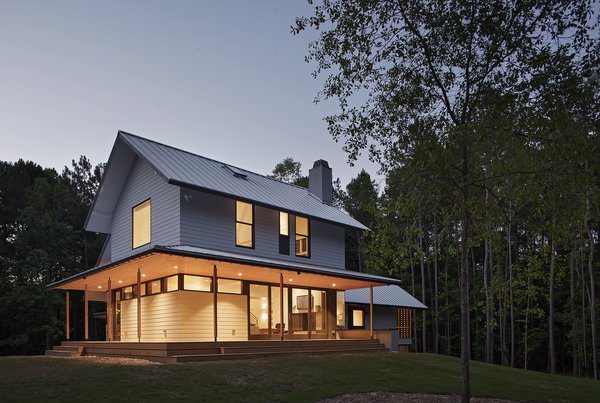 “The main volume presents a traditional front and is wrapped on the west and south by a deep porch,” says architect Erin Sterling Lewis. “Living and dining spaces access the porch.” A standing seam metal roof with a Kynar finish and HardiePlank Lap Siding cover the exterior of this 3,000-square-foot home. Photo of The Farmhouse modern home