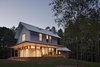 “The main volume presents a traditional front and is wrapped on the west and south by a deep porch,” says architect Erin Sterling Lewis. “Living and dining spaces access the porch.” A standing seam metal roof with a Kynar finish and HardiePlank Lap Siding cover the exterior of this 3,000-square-foot home. Photo of The Farmhouse modern home