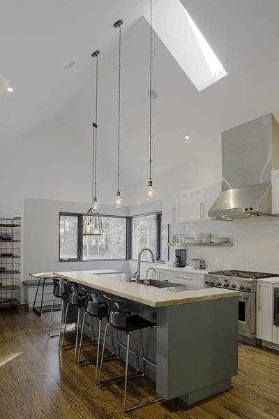 “Knowing that the kitchen would be where the family would spend most of their time, it was designed to have a variety of seating and really good views to the beautiful forest and field outside,” says Lewis. IKEA bar stools line up against white quartz countertops, and lighting by Schoolhouse Electric & Supply Co. shines overhead. Photo 4 of The Farmhouse modern home