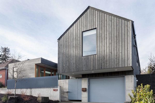 The cedar-clad front facade features one of the home’s defining design elements: a cantilevered gable that appears to float over the garage. The project is composed of two unique forms, divergent in convention but complementary in execution. A traditional gable, simplified and modernized, sits next to a striking modernist cube. A custom entry gate fabricated by Dovetail’s metal shop and a steel privacy fence add color to the front elevation. Photo of Central District Residence modern home