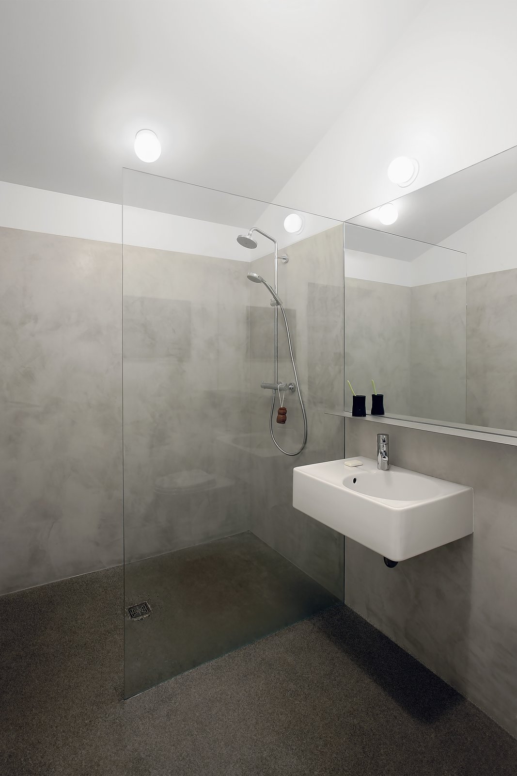 Milestones' cement plaster covers the walls of the minimalist bathroom. The Scola sink from Duravit is accompanied by a chrome Grohe Essence faucet and Hansgrohe's Croma Green Showerpipe.