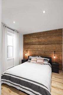 8 Beautiful Home Projects Using Reclaimed Wood - Photo 4 of 8 - In a project in Quebec, Canada, a 1924 building was renovated by Bourgeois Lechasseur Architects. The renovation sought to modernize the apartment while preserving the historical elements—in particular, reusing wooden boards that were salvaged during demolition. The unfinished boards act as a rustic, earthy accent wall and headboard, while the surrounding white walls and crisp bed linens keep the room contemporary.