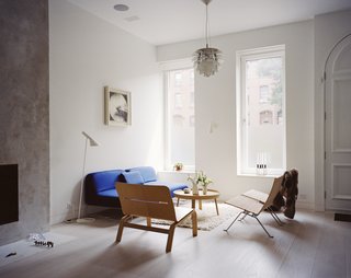 The living room is furnished with rattan chairs from Fritz Hansen, a Muuto side table, an Artichoke pendant by Poul Henningsen for Louis Poulsen, and a blue Living Divani sofa, one of a few color-popping accents found throughout.