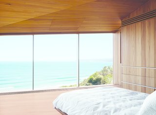 This Surfer Rules the Ocean from a Cliffside House - Photo 7 of 9 - The couple, both surfers and beach lovers, wake up to stunning views of the azure-blue Southern Ocean in their otherwise monochromatic eucalyptus master bedroom. Wardle's firm designed the bed base, and the panel in the ceiling hides a television.