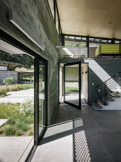 Retirement Never Looked Better and More Sustainable - Photo 5 of 10 - The entrance to the main pavilion is defined by a pivoting glass door from Fleetwood (above left). The stairs lead to the media loft, where Inga Sempé’s Ruché sofa for Ligne Roset breaks up the gray. Among the couple’s few directives were tall ceilings, which Feldman covered in low-cost plywood sheets.