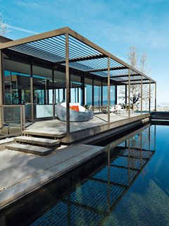 The house’s slatted, anodized aluminum canopies and indoor-outdoor spaces flow into one another. The resin Opal lounge and Square Cube table, with pillows and cushions covered in Sunbrella fabrics, and the teak and powder-coated cast aluminum Silver Dining swivel rocker, are all from the Veneman Collections. Image courtesy of Jill Paider.