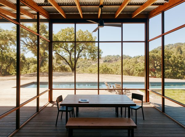 10 Enclosed Porches That Are Put to Good Use - Photo 6 of 10 - In line with the family’s active lifestyle, the kitchen is also situated outside. To the south of it, a screened-in area off the porch, clad in ipe and black fiberglass mesh, serves as the impromptu dining area. The table and chairs are from Black’s Farmwood, and the ceiling fan is by Fanimation.