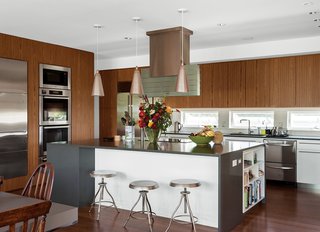 In the kitchen, teak-and- thermofoil cabinets and Caesarstone countertops mix with Miele appliances—wall ovens, induction cooktop, hood, and microwave—and a Sub-Zero refrigerator. The kitchen sink and faucet are by Blanco. The owners, who split their time between Fishers Island and Great Britain, found the vintage pendant lamps at Lassco architectural salvage. 