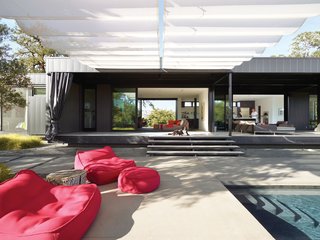 When Prefab Is Painless - Photo 2 of 7 - In the foreground are Float beanbag chairs and poufs from Paola Lenti. Mamagreen sofas nestle near the house on the sun-dappled deck. A 9.5-foot-tall shade cloth curtain seals off the entire length of the house when the couple is away, keeping the heat out of the interior and preventing accidental bird suicides against the floor-to-ceiling glass walls.