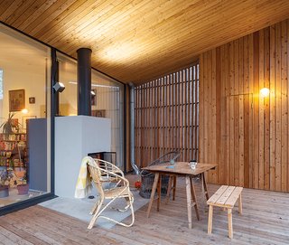 This Home Will Make You Want to Build Your Own Sauna - Photo 9 of 10 - A collection of vintage furniture, including a rattan armchair and a drafting table, is gathered around the terrace fireplace, which shares a volume with the hearth in the adjacent living room behind. Outdoor sconces are from iGuzzini.