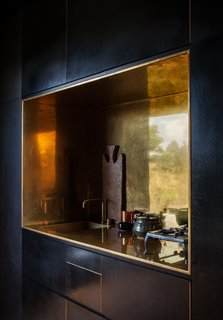 The kitchen’s brass-lined niche, with a matching tap by Arne Jacobsen for Vola, contrasts the otherwise spare, black formply interior of one of the cabins. "We wanted to introduce one piece that was deliberately special, that would build drama between the humility of the unfinished and the very precise polish of this one object," says designer Nat Cheshire.