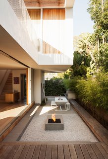 The outdoor living room serves as both a counterpoint and extension of the interior, with amenities that include a Gandia Blasco dining table and bench, a Lynx grill, and a custom concrete fire pit designed by Kathleen Ferguson; it sits atop a bed of crushed white rock. A built-in bench runs along the length of the courtyard.