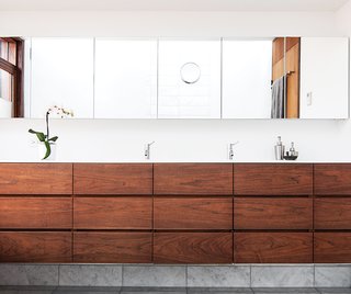 Architect Paul Syme designed custom storage units with dark-stained walnut fronts that provide a place for everything in his clients’ Toronto bathroom. The wall-to-wall mirror and the Corian counter are custom, and the faucets are by Vola.