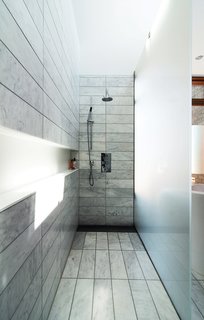 The standing shower is set off by etched-glass panels supported by stainless-steel hardware. There is no threshold; instead, the tile within the shower zone slopes down very slightly to a floor trough with a custom stainless-steel grille. Along the wall, a Corian shelf—"the longest soap dish in the world," resident Don Evans jokes—runs the length of the space. 