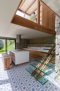 In the kitchen, a staircase with a wood backbone supports floating glass treads. The home’s main entrance is located on the top level due to the property’s incline.