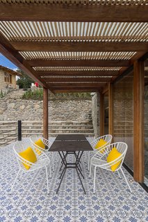 Visitors cross a tile deck underneath a pergola to enter. 