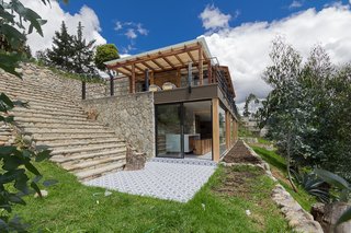 The exterior defers to the local vernacular and landscape. The roof is made of exposed wood and handmade clay shingles. Structural walls from an earlier construction project were discovered onsite and form the basis for the stone barrier and stairs that hug the bank. The architects took care not to disturb the local shrubs and vegetation. 