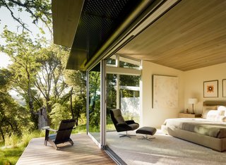 A Meadow With Amenities - Photo 9 of 10 - Sloped ceilings, covered with stained Western red cedar, add warmth to the interior (bottom). "We set out to design using the best of what modernism has to offer, but to try to execute that in a way that is livable and home-like," says architect Jonathan Feldman. The bedroom contains an A. Rudin bed and a Beau chair from Room & Board. It opens onto a deck with an aluminum awning.