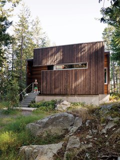 The facade is clad with beveled siding, stained dark to meld into the forest. 