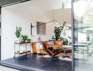 This Los Angeles Home is Driven by Automotive Design - Photo 5 of 9 - A love of midcentury design marks the couple’s choice of living room furnishings, which include an Eames lounge chair and a Noguchi coffee table, paired with a sofa from HD Buttercup. The arching neck of the Prouvé Potence sconce mirrors the home’s exterior form, while the large Fleetwood sliding door extends the space to the outdoors.
