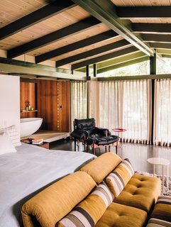 A tub zone lined in redwood connects to the master bedroom, which is furnished with a vintage Sergio Rodrigues lounge chair and Voyage Immobile seats from Roche Bobois.