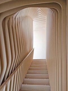 What’s the Twist Behind This Home’s Sinuous Staircase? Ordinary Plywood - Photo 8 of 14 - <span style="line-height: 1.8;">Organic, undulating forms frame the stairwell that connects the first floor and garden floor. </span>Though they give the appearance of bent plywood, each curved layer of the ribbed corridor was constructed with flat, laminated cutouts, including the rounded hand rail. 