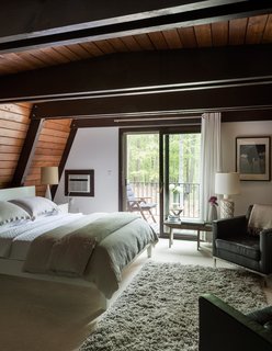 The residents sleep beneath Douglas fir beams that they darkened using a mix of Ebony and Moorish Teak wood stain by Zar. In front of a small balcony is an early American farm bench purchased at the Rhinebeck Antique Fair. The Gaser rug is from IKEA. 
