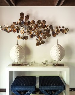 Nearby, the Lacquer Console Table holds a pair of Ceramic Tortoise Shell lamps and conceals a Double X bench, also by the designer (below). The brass Raindrops wall sculpture, a reissue of a midcentury metalwork by C. Jeré Studio, is from JA Finds, Adler’s curatorial venture. 
