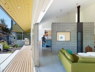 A Suburban Vancouver Home Edits its Privacy Settings - Photo 1 of 5 - Sliding doors by Mountainview unite the garden and interior of a residence in British Columbia. The underside of the deck overhang is covered in Benjamin Moore’s Turmeric paint, a shade also used on the house’s front facade. A Canyon sofa by Bensen joins Fat Fat tables by Patricia Urquiola for B&B Italia in the living room; a cinderblock wall with a stove by Stûv divides the space from the kitchen.