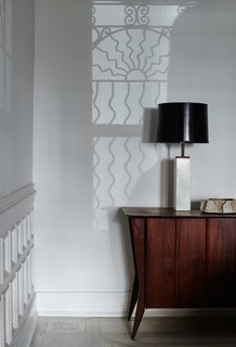 Graphic, curvilinear shadows cast from an original window grate play with geometrically stark furnishings, including the vintage lamp and midcentury Danish credenza in the family room.