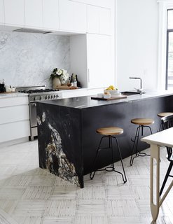 Matte-black quartzite slabs from ABC Worldwide Stone form the kitchen island, which is outfitted with Blanco fixtures; a white Carrara backsplash frames the Bertazzoni range and Dunsmuir cabinetry. The oak-and-steel bar stools are from ABC Carpet & Home.