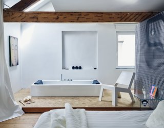 A spare layout marks the master suite on the third floor. The rectangular KOS bathtub, integrated into an elevated plywood platform, pairs with Gert Van Der Vloet’s Cut Low lounge in Corian. The couple used elements of a photo they took of one of Venlet’s designs to create the graphic wall covering. 