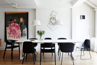 A series of black Muuto chairs—Fiber, Cover, Nerd, and Visu—surrounds a 70/70 table and white Ambit pendants, both by TAF Architects for Muuto. 