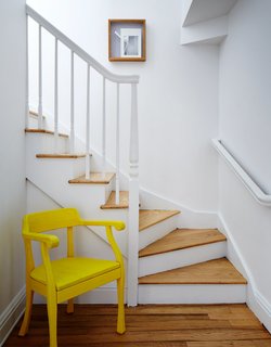 In the hallway, a yellow Raw chair by Jens Fager for Muuto pops against the white staircase.
