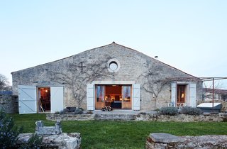 Designers Russell Pinch and Oona Bannon kept many of the architectural details of the 300-year-old cow barn they turned into a second home, including its terra-cotta roof tiles. The primary structural change took place on the front facade, which they tore down and rebuilt, opening space for a traditional oeil-de-boeuf window. The door on the left opens to a workshop. In addition to designing furniture, the couple also create interiors for select clients.