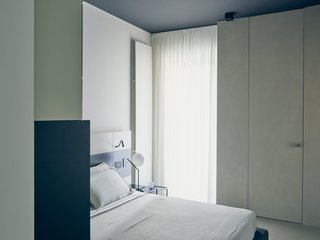 A custom lacquered-wood headboard with built-in task lights by MLE complements a Pianca bed in the master bedroom. An IC Lights T lamp by Michael Anastassiades for Flos offers additional illumination. 