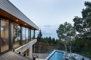 A Home Inspired by the Stars Soars Off the Ground - Photo 3 of 5 - The second floor includes another open plan that blends the kitchen, dining area, and living room together. After ascending to the top, another deck folds over the pool to create an overhang. The wide-spanning glass wraps around the top of the cantilever to take full advantage of the natural setting. 