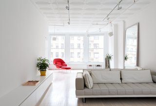 This 60-Square-Foot Structure Divides and Conquers in a Manhattan Renovation - Photo 3 of 8 - A linear lacquer storage unit with a Corian top helped define the main living areas; now the residents spend more time enjoying the apartment’s northern exposure–one of two main sources of natural light in the floor-through loft. A custom whitewashed oak mirror, White paint by Benjamin Moore, and a lighting program by Melanie Freundlich carry the brightness throughout the loft. The Grid sofa is by Resource Furniture.