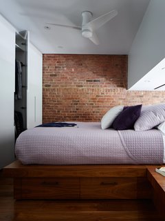 A variation on the system serves as a wardrobe in the sleeping loft. Additional storage can be found in the walnut platform with side tables. Although it appears less in the photo, the space between the platform and the lowest part of the ceiling is about four and a half feet, allowing René to comfortably sit up in bed. A Lutron screen lowers for privacy. 