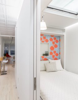 Across from it, a Murphy bed by Resource Furniture—lined with Camilla Meijer wallpaper and featuring a customized niche—allows the space to function as a guest room. An electric Velux skylight frames views of the original tin plates above. The architects chose to leave space between the top of the structure and the ceiling to maintain the rectangular proportions of the loft. "It reads right away," Singer says of the volume. "It’s very satisfying."