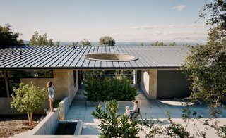Resident Elizabeth Twaddell enjoys the weather with her daughter Uma outside the guesthouse Neal Schwartz designed for her mother-in-law, Surendra, who frequently visits for extended stays. A concrete driveway forks off from the main house to lead to a covered breezeway, sited between the new 775-square-foot structure and a two-car garage. 