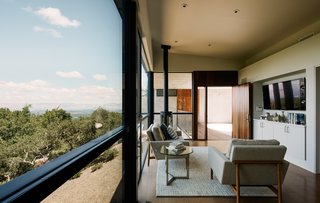 Zoning laws determined the maximum square footage of the guesthouse; as a workaround, Schwartz created a detached two-car garage, which did not count toward the dwelling’s overall size. In addition to the breezeway and the overhang, a series of ipe slats unite the two structures, covering the doors and a walkway in between. The living area is furnished with a Raleigh sofa and armchair by Jeffrey Bernett and Nicholas Dodziuk; the direct-vent gas stove is by Jøtul. 