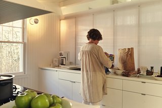 Damaged by Superstorm Sandy, a Fire Island Cottage is Rebuilt - Photo 1 of 6 - .In the galley-style kitchen, Ann sorts groceries into Akurum cabinets from IKEA. For the sconces, the architects selected generic porcelain sockets, then stylized them with silver-cap bulbs. 