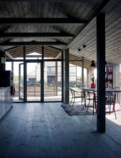 With its timber rafters and expanses of glass, the house contrasts with its more conventional neighbors. To keep the focus on the views, Anna opted for minimal furnishings. The final design is the result of many imagined interiors, she explains: "I dreamt about this house for some time—then I saw it in real life." In the dining area, a pair of IKEA Hektar pendants hangs over a table designed by Anna’s employees as a gift. The chairs are from European home improvement store Obi; the rug is vintage.