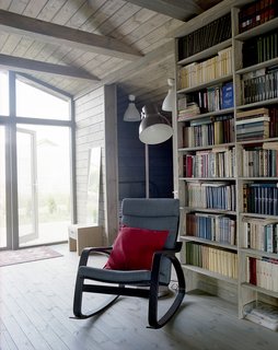 Near a Gent wood-burning stove by Thorma in the living area, an IKEA Poäng chair and ottoman provide a cozy spot for reading. Thanks to the passive design strategies utilized by Ovchinnikov, the house stays warm through the winter with only minimal heating required.